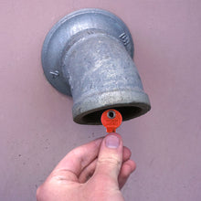 Load image into Gallery viewer, 50692 Magnetic Key, M1-69 Red - Hand Holding Red Magnetic Key Next to a Drain Pipe