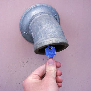 50773 Magnetic Key, WR5-67 Blue - Hand Holding a Blue Magnetic Key Next to a Drain Pipe