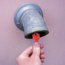 Load image into Gallery viewer, 50772 Magnetic Key, WR5-67 Red - Hand Holding Red Magnetic Key Next to a Drain Pipe